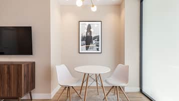 Een moderne kamer met een televisie, een ingelijst kunstwerk, twee witte stoelen, een ronde tafel en een houten kast.