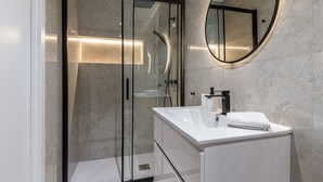 Ein modernes Badezimmer mit einer gläsernen Duschkabine, einem weißen Waschbecken und einem runden Spiegel.