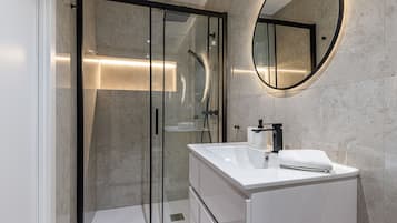Een moderne badkamer met een douchecabine van glas, een wit wastafeltje en een ronde spiegel.