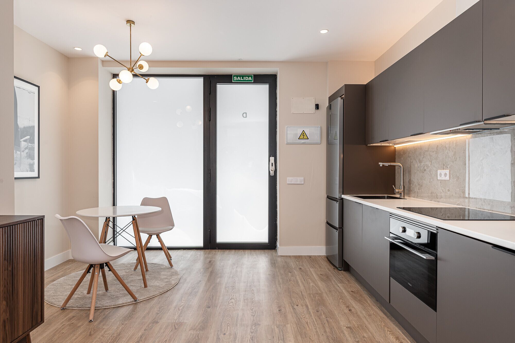Een moderne keuken met een inbouwoven, een spoelbak en een eethoek met tafel en stoelen.