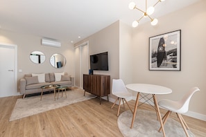 A modern living room with a sofa, coffee table, TV, and a dining area with chairs and a table. - Waou Essence I Bernabeu - Short Term Rental (Madrid)