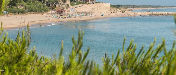 A beach with people, umbrellas, and a building in the background. - Felicia: Cozy Apartment with Terrace near the Beaches of L’Escala (L'Escala)