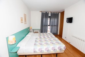 A bedroom with a bed, a desk, a chair, a TV, and a window with curtains. - HOSTAL VIA LACTEA (Burgos)