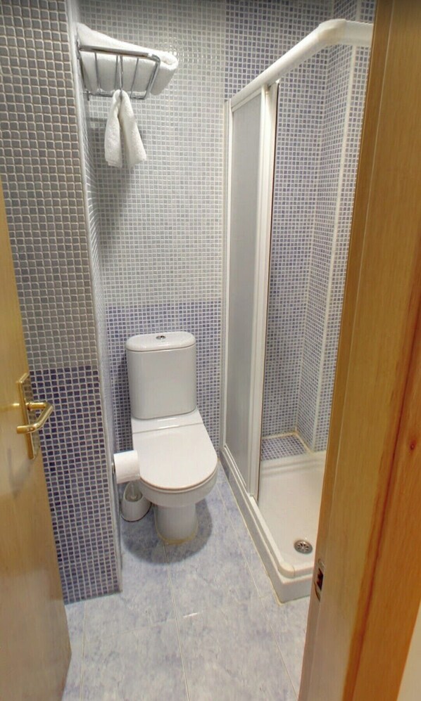 A bathroom with a toilet, a shower, and a tiled floor. - HOSTAL VIA LACTEA (Burgos)