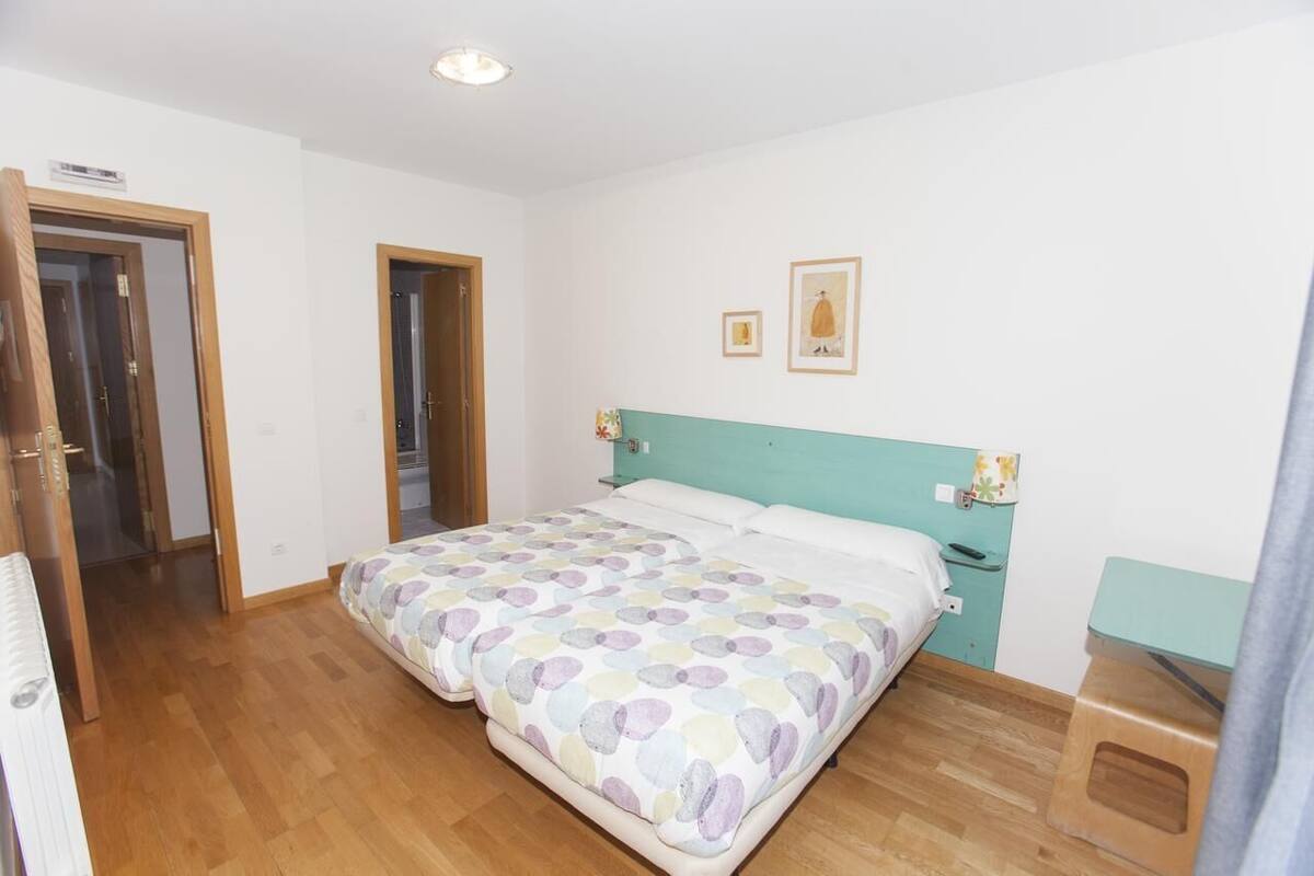 A bedroom with a bed, a nightstand, a wooden floor, and a door.