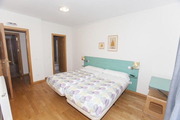 A bedroom with a bed, a nightstand, a wooden floor, and a door. - HOSTAL VIA LACTEA (Burgos)