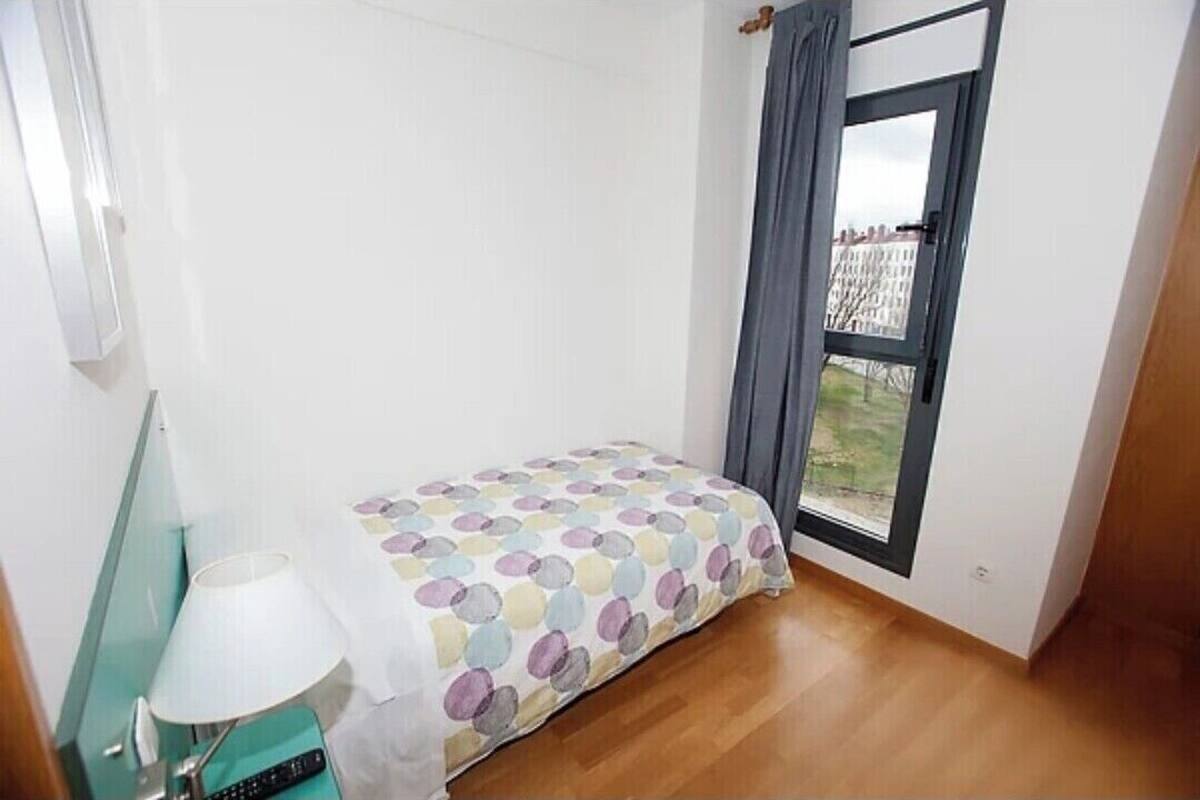 A small, bright room with a bed, a lamp, and a window with curtains.