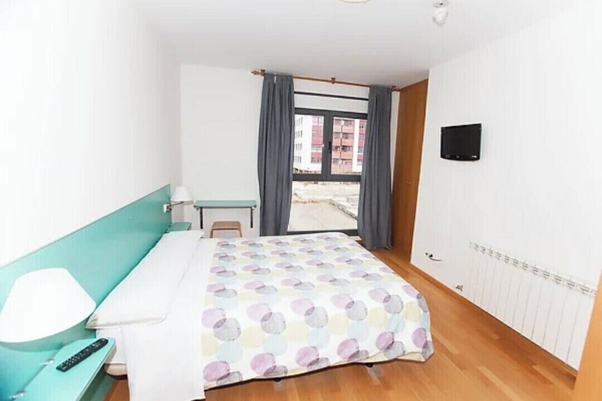 A hotel room with a bed, a desk, a chair, a TV, and a window with curtains.