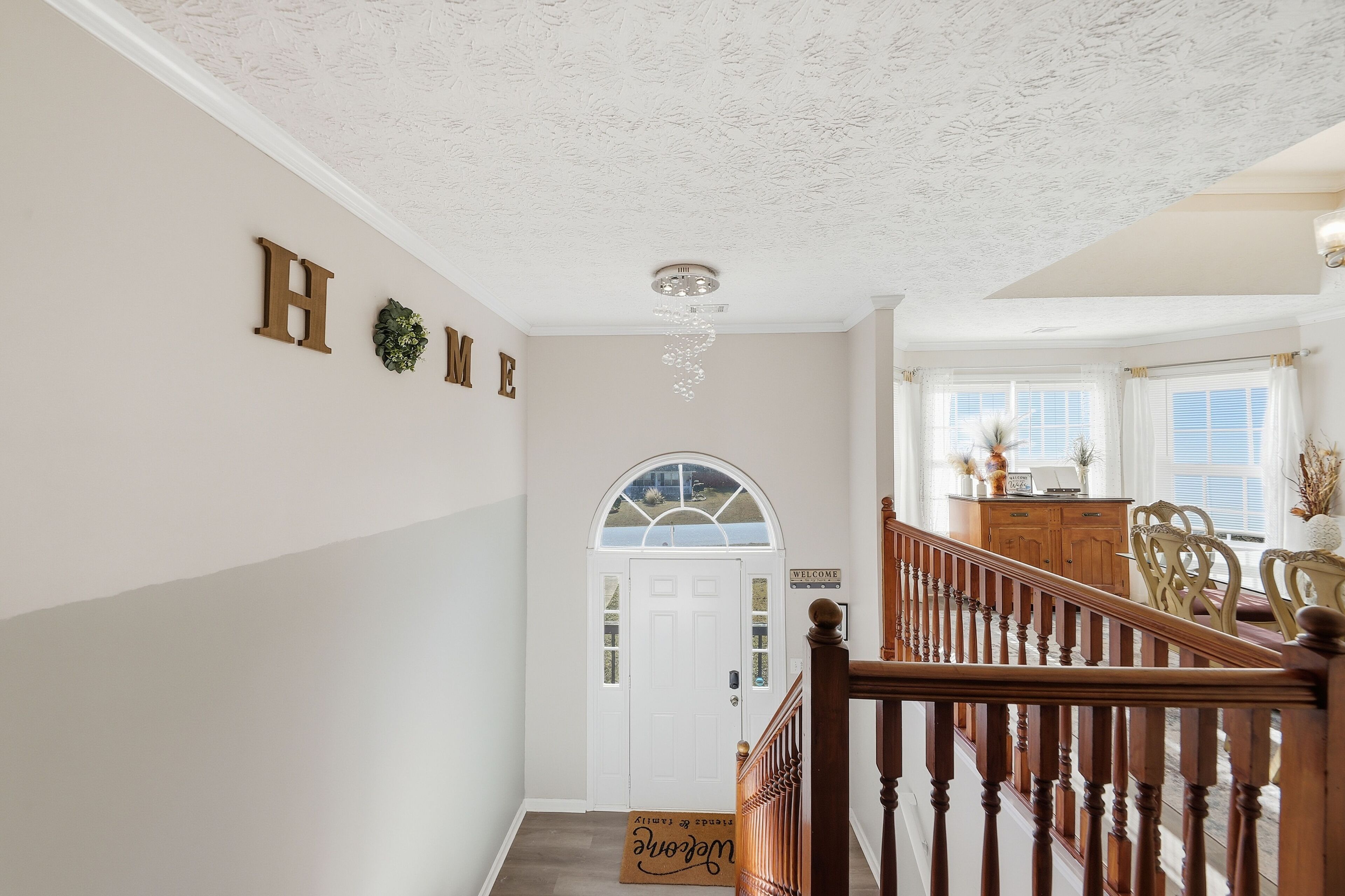 Un pasillo con una escalera de madera, una puerta blanca con un letrero que dice 'Welcome' y un letrero con la palabra 'Home' en la pared.