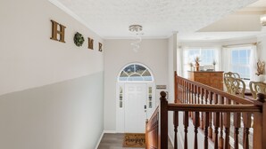 Un couloir avec un escalier en bois, une porte blanche sur laquelle est inscrit le mot « Bienvenue », et une pancarte « Chez nous » accrochée au mur.