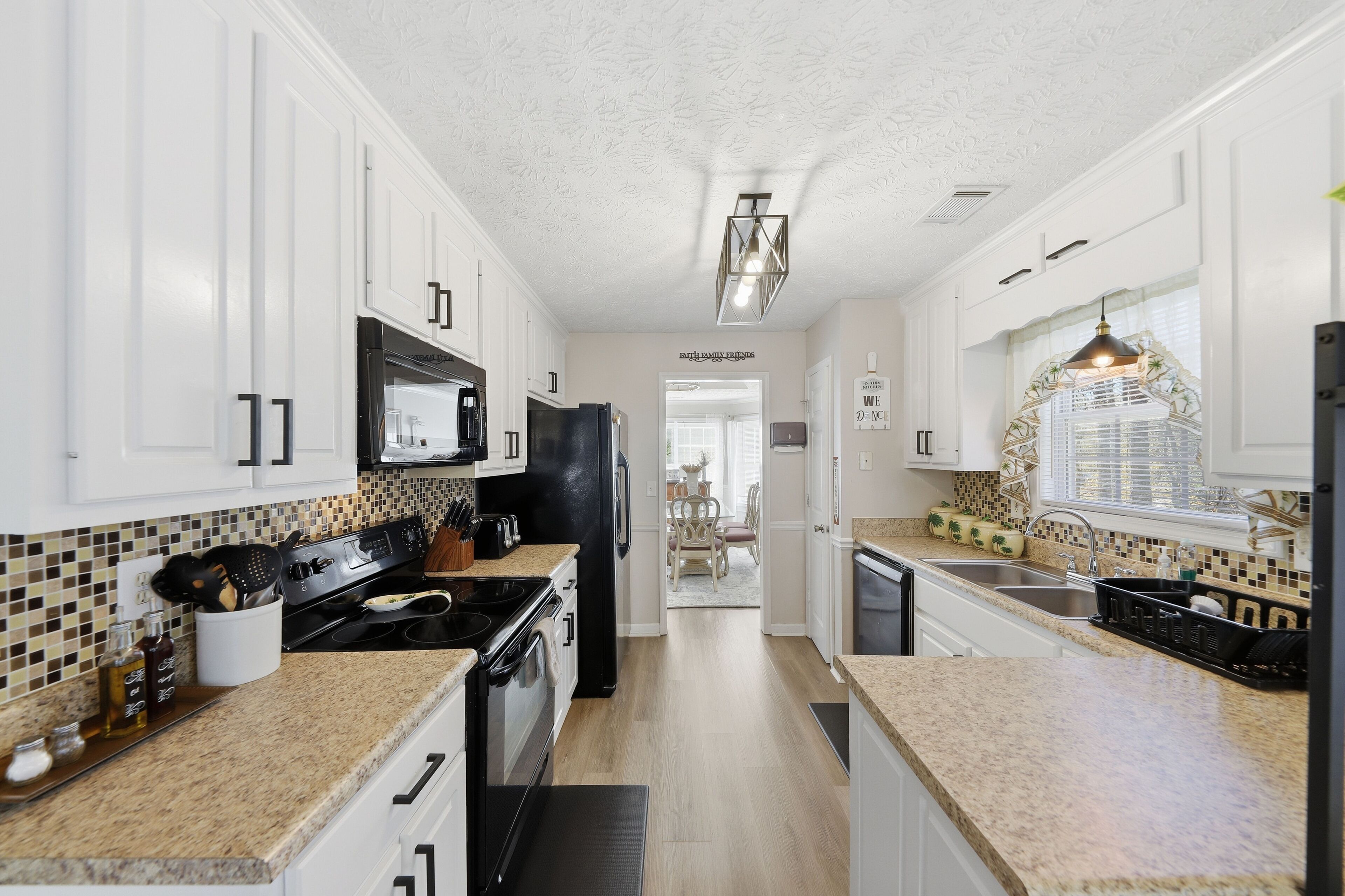 A modern kitchen with white cabinets, a black refrigerator, and a granite countertop.