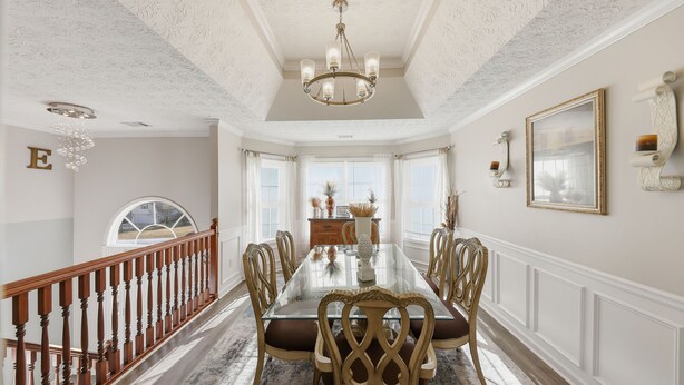 Une salle à manger avec une table en verre, des chaises en bois, un lustre et une vue par la fenêtre.