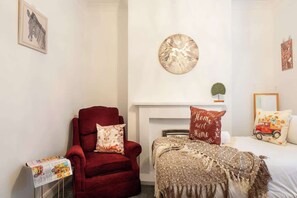 A bedroom with a red armchair, a bed with a patterned blanket, a fireplace, and wall art. - 4 Bedrooms Home Close to Shops, A63 Saltend Hull (Kingston Upon Hull)