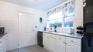 Cocina con alacenas blancas, lavavajillas, un lavamanos y una ventana con una planta.