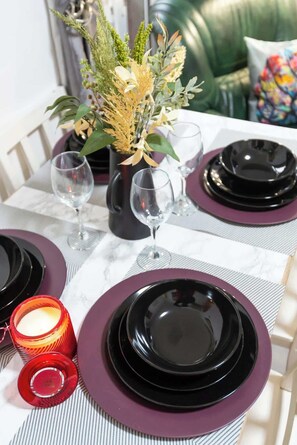 A table set with black plates, purple napkins, and clear glasses, accompanied by a vase of flowers and a lit candle. - 4 Bedrooms Home Close to Shops, A63 Saltend Hull (Kingston Upon Hull)