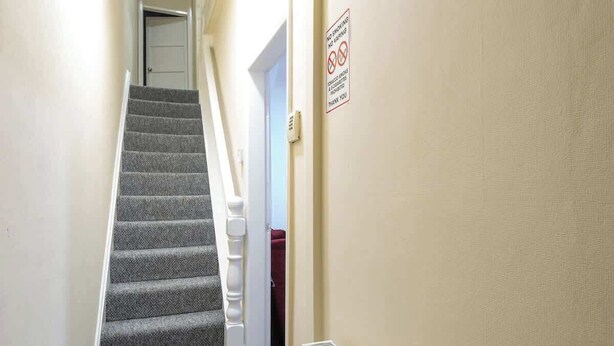 Una escalera alfombrada con barandilla, una puerta en la parte superior y un cartel de prohibido fumar en la pared.