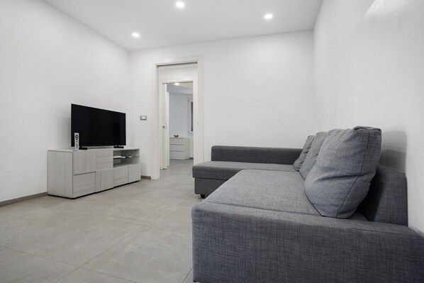 A modern living room with a grey sofa, a flat-screen TV on a wooden cabinet, and a hallway leading to another room.