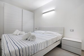 A modern bedroom with a bed, a nightstand, and a wall-mounted light fixture.