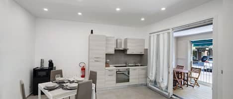 A compact kitchen with modern appliances, a dining area with chairs, and a view through a glass door.
