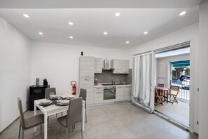 Una cucina compatta con elettrodomestici moderni, un'area pranzo con sedie e vista attraverso una porta vetrata.