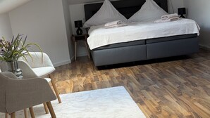 Un dormitorio con una cama, una silla, una mesita, una planta y un tragaluz.