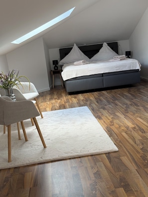 Une chambre à coucher avec un lit, une chaise, une petite table, une plante et une lucarne.