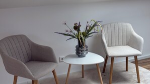 Dos sillas con patas de madera y una mesa blanca con un jarrón de flores.