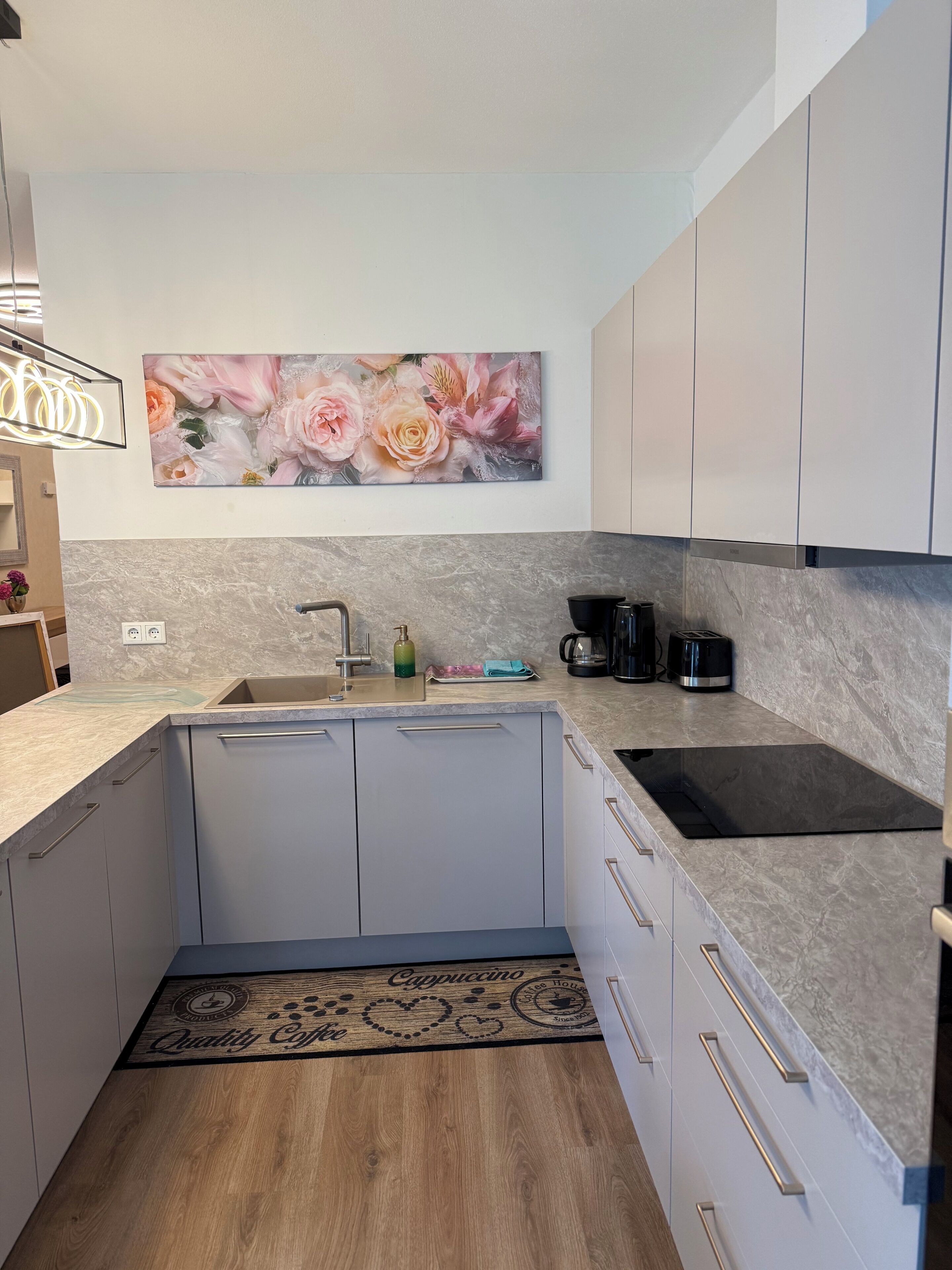 Eine moderne Küche mit Marmorarbeitsplatte, Spüle, Kaffeemaschine und einem Wandbild mit Blumenmuster.