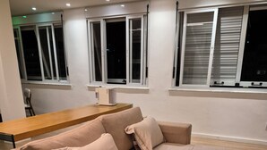 Un dormitorio moderno con un sofá cama, una mesa de madera y dos ventanas con persianas.