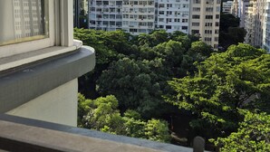 Vista desde una ventana que da a un paisaje urbano con edificios de varios pisos, árboles verdes exuberantes y una montaña destacada al fondo.