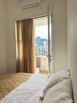 A hotel room with a bed, a window with curtains, and a view of buildings and mountains. - Penthouse in Copacabana, one block from the beach, with views of the ocean and Christ the Redeemer. (Rio de Janeiro)