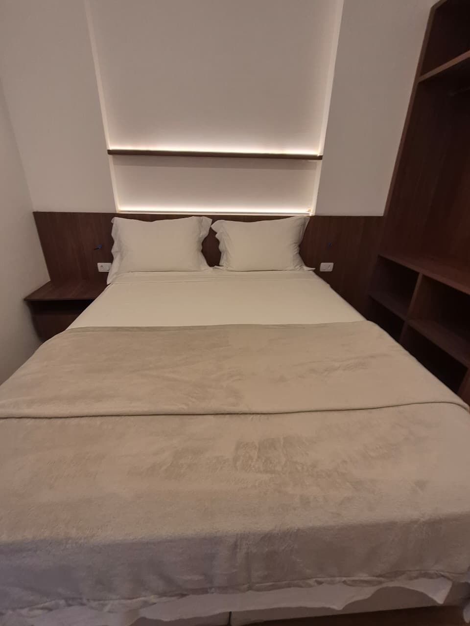 Een bed met hoofdbord, nachtkastje en een kledingkast.