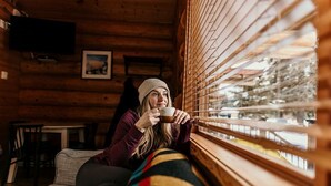 A person sitting by a window in a log cabin with wooden walls, a television mounted on the wall, and a framed picture on the wall. - Riverside RV Resort (Whistler)