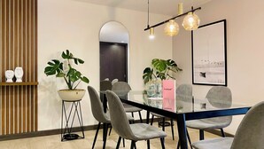 Un comedor moderno con una mesa de vidrio, sillas tapizadas grises, una planta en maceta y una lámpara colgante.