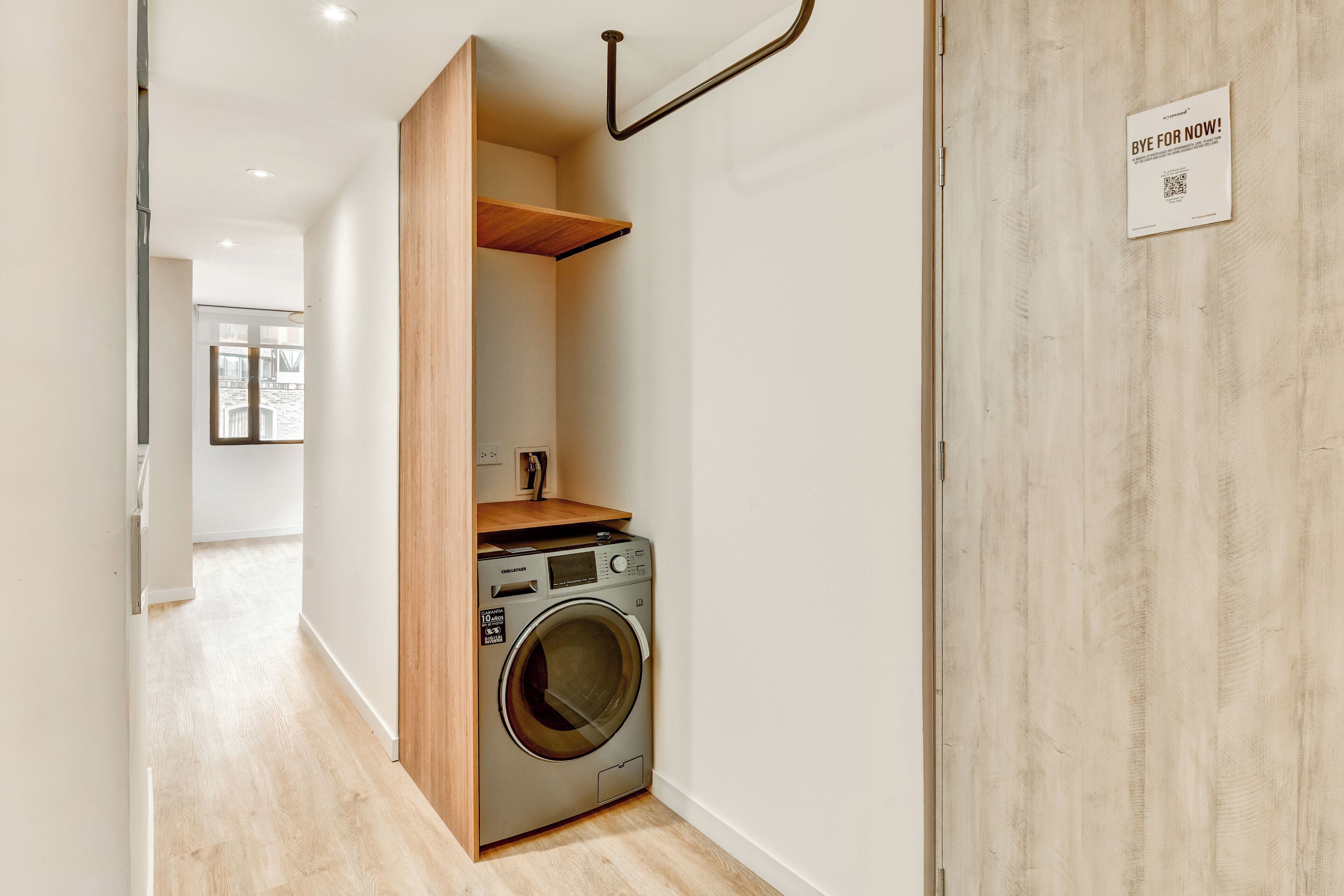 Une buanderie équipée d’un lave-linge, d’étagères en bois et d’une porte avec une pancarte.