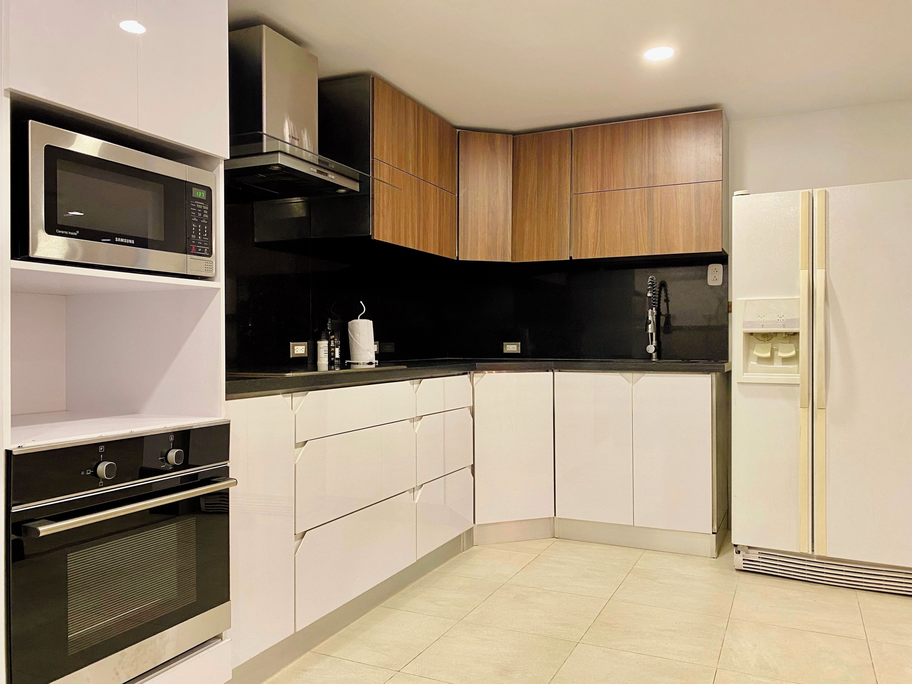 A modern kitchen with white cabinetry, a built-in oven, a microwave, and a refrigerator.