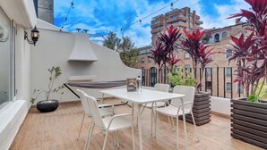 Un patio en la azotea con una mesa y sillas blancas, una maceta negra y una planta en maceta.