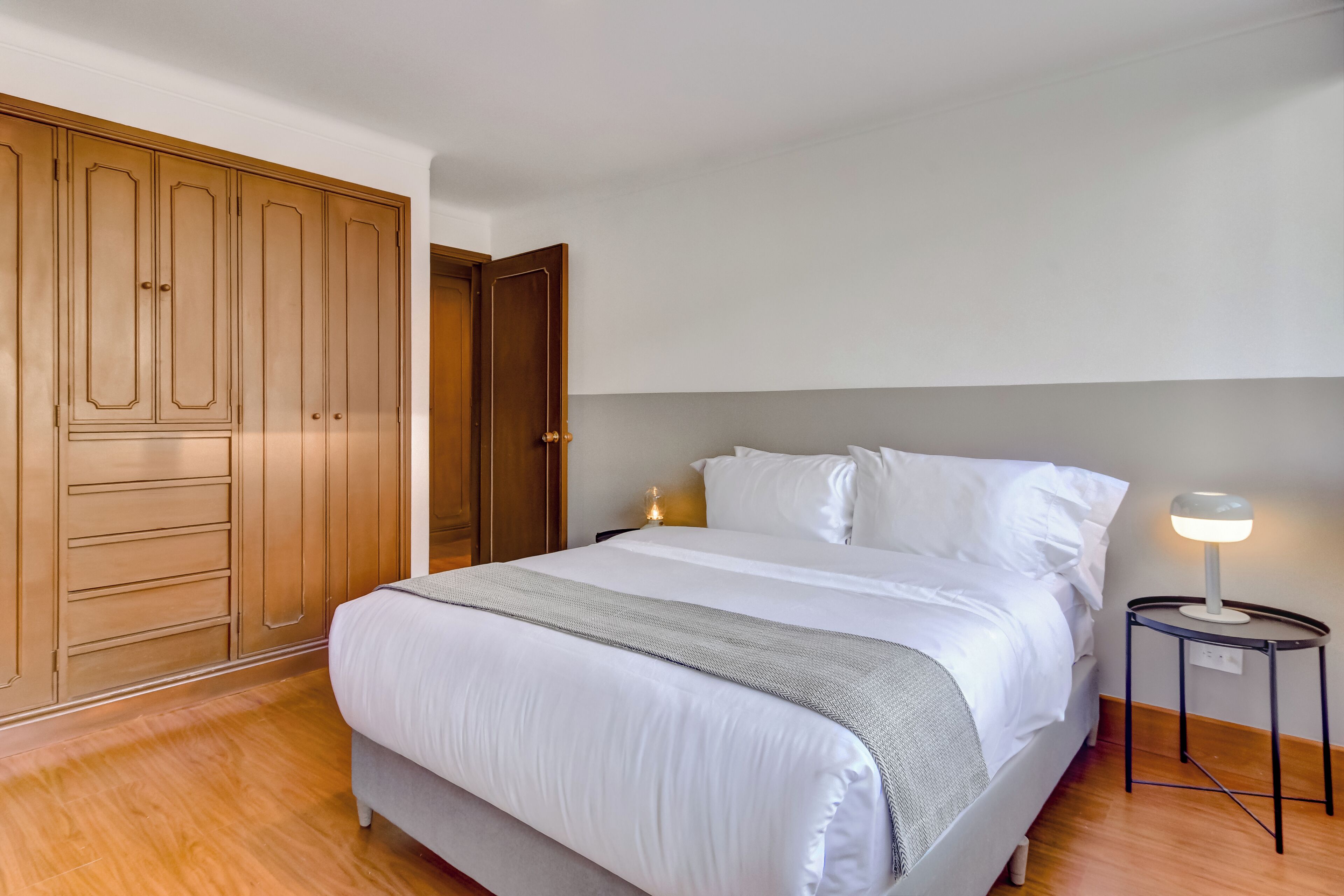 Ein Schlafzimmer mit Bett, Holzschrank, Nachttisch und Lampe.