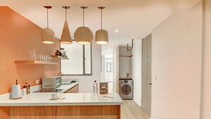 Una cocina moderna con una isla central, iluminación colgante y una lavadora al fondo.