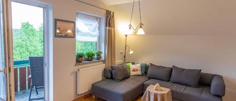 A cozy living room with a grey sofa, a small table, and a window with plants.