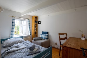 Une chambre à coucher avec un lit, une chaise en bois, une petite table, une fenêtre avec des rideaux et une bibliothèque.