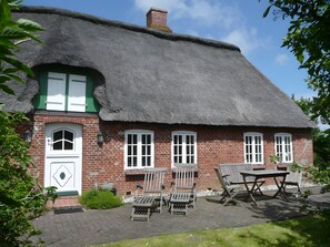 Une maison traditionnelle en briques, avec un toit de chaume, une porte verte et une cheminée en briques.