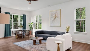 Una sala moderna con un sofá gris, sillones blancos, una mesa redonda y un comedor con una mesa y sillas.