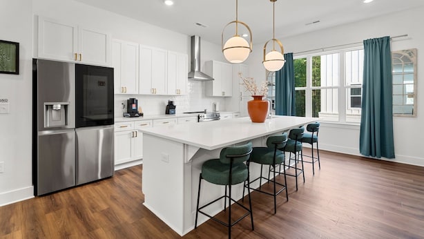 Una cocina moderna con armarios blancos, electrodomésticos de acero inoxidable, una isla grande con taburetes de bar e iluminación colgante.