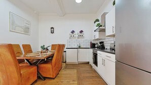 Cozinha moderna com armários brancos, geladeira de aço inoxidável e área de jantar com cadeiras de couro.