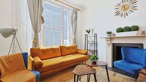 Uma sala de estar com sofá, poltronas, uma mesinha e lareira.
