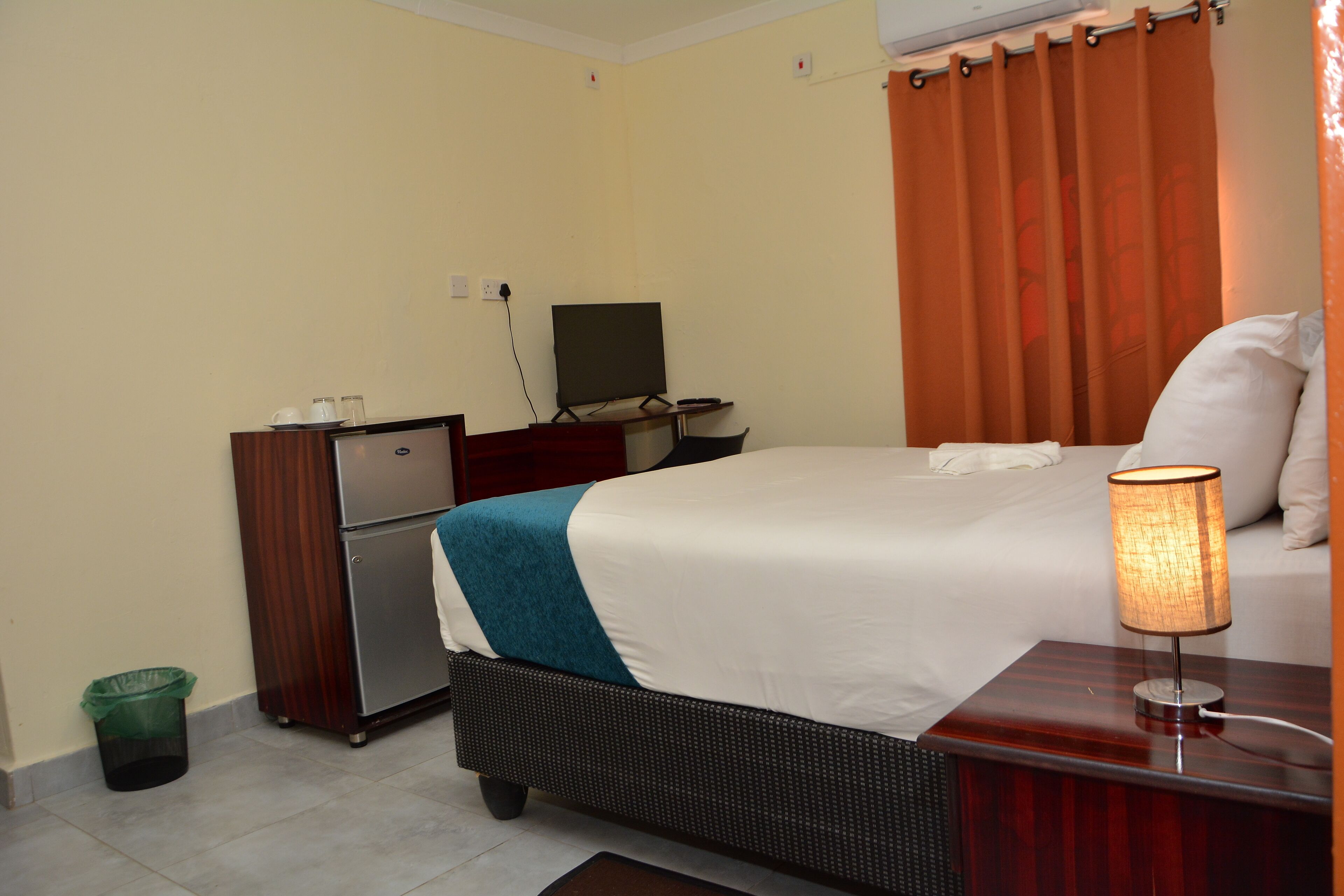 Ein Hotelzimmer mit Bett, Schreibtisch, Computer, Papierkorb und Vorhang.