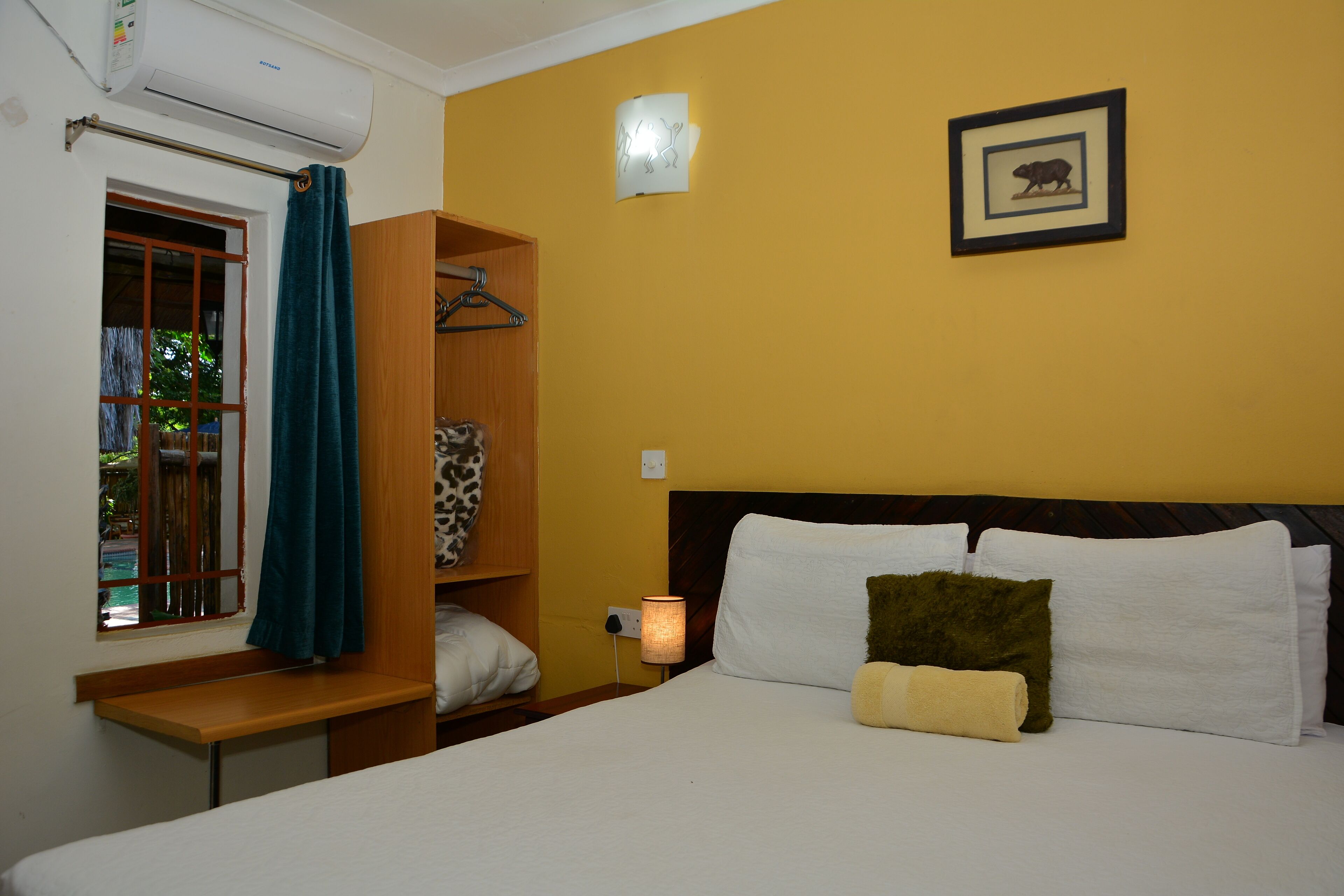 A hotel room with a bed, a nightstand, a lamp, a window with a curtain, a wardrobe, and a wall-mounted picture.