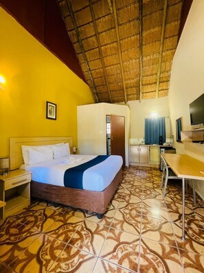 A hotel room with a bed, a desk, a television, and a bathroom door.