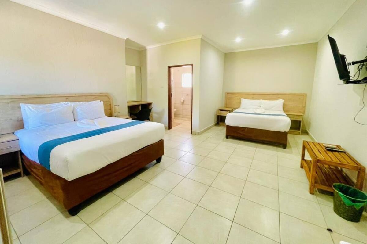A hotel room with two beds, a television, a wooden table, and a green bucket.